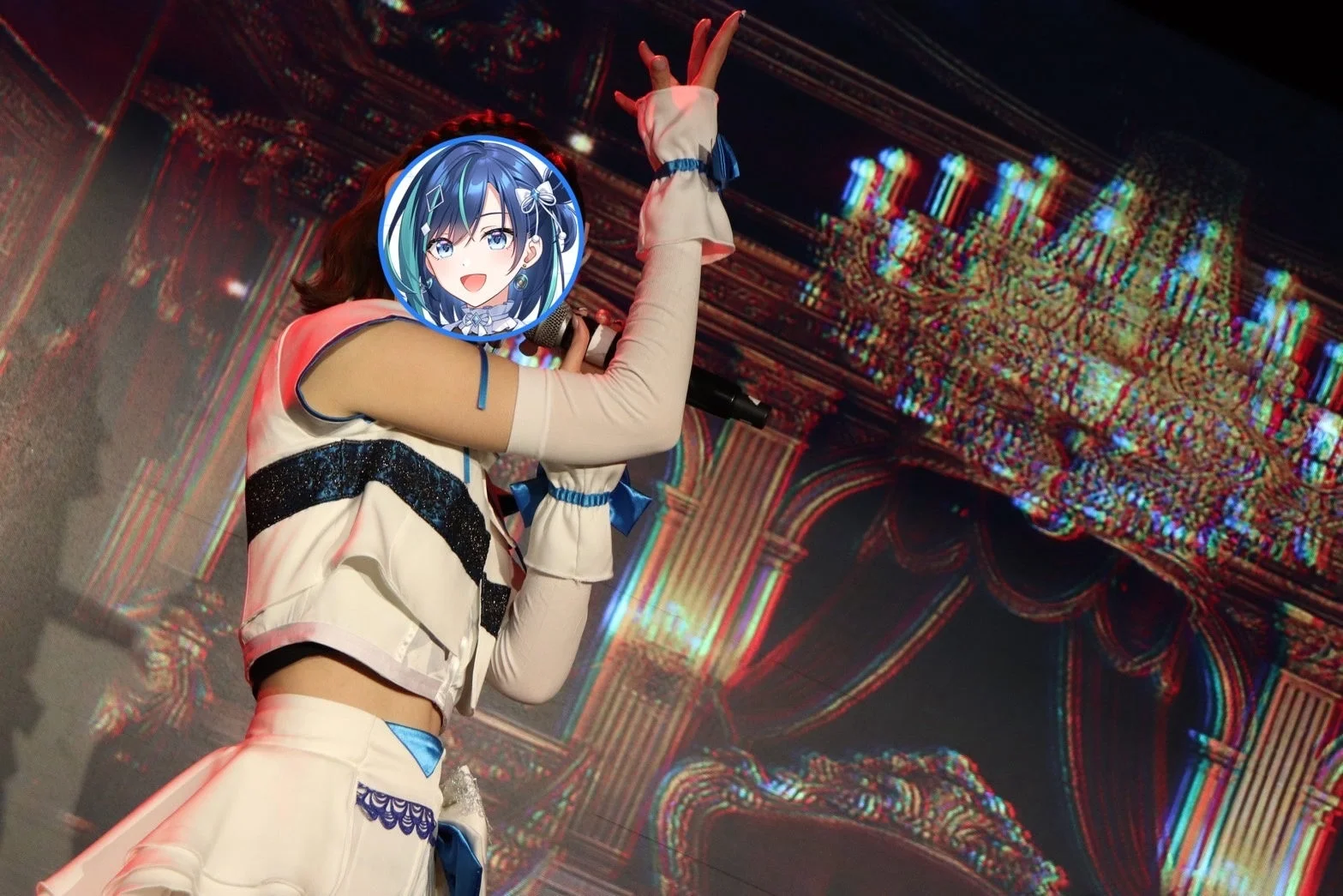 白と青のアイドル衣装をまとったパフォーマーがマイクを手にステージで歌唱している様子