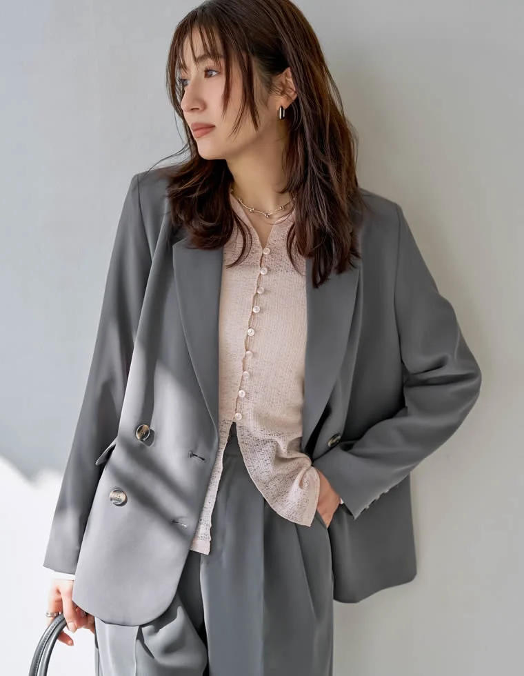 グレーのダブルブレストジャケットとパンツ、淡いピンクのシアーなカーディガンを合わせた女性のファッション写真
