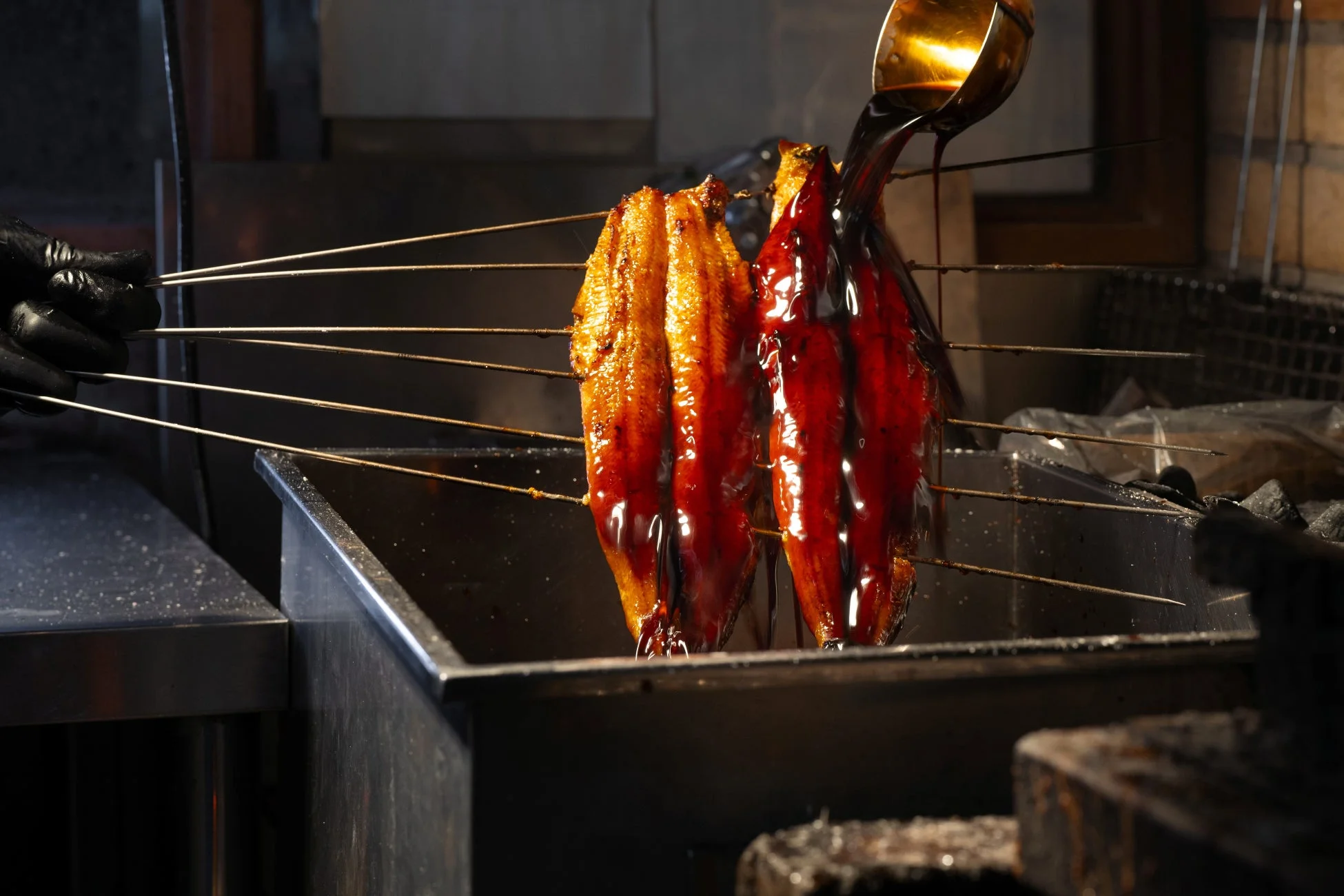 炭火で焼かれたうなぎにタレが塗られている画像