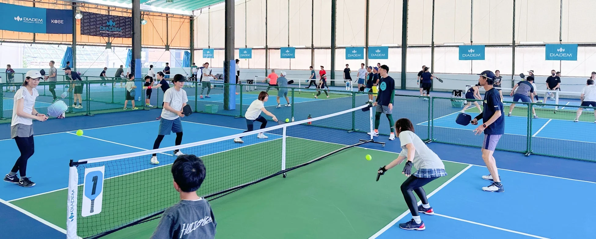 青と緑のコートで多くの人々がピックルボールを楽しんでいる屋内スポーツ施設の様子