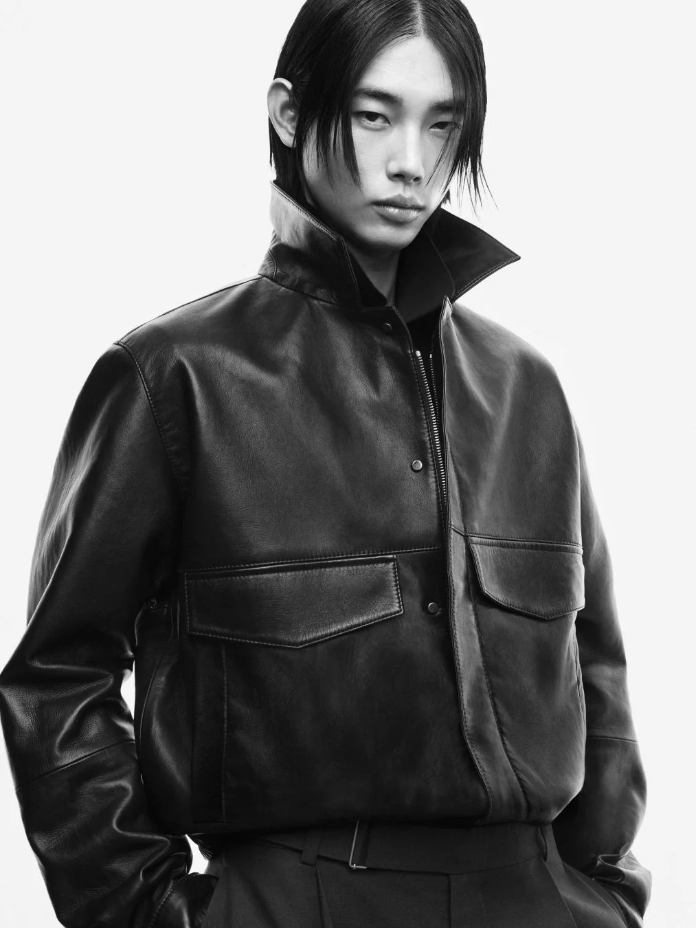 黒いレザージャケットを着用した長髪の男性モデルが写るモノクロのポートレート。クールな表情が印象的なファッション写真です。