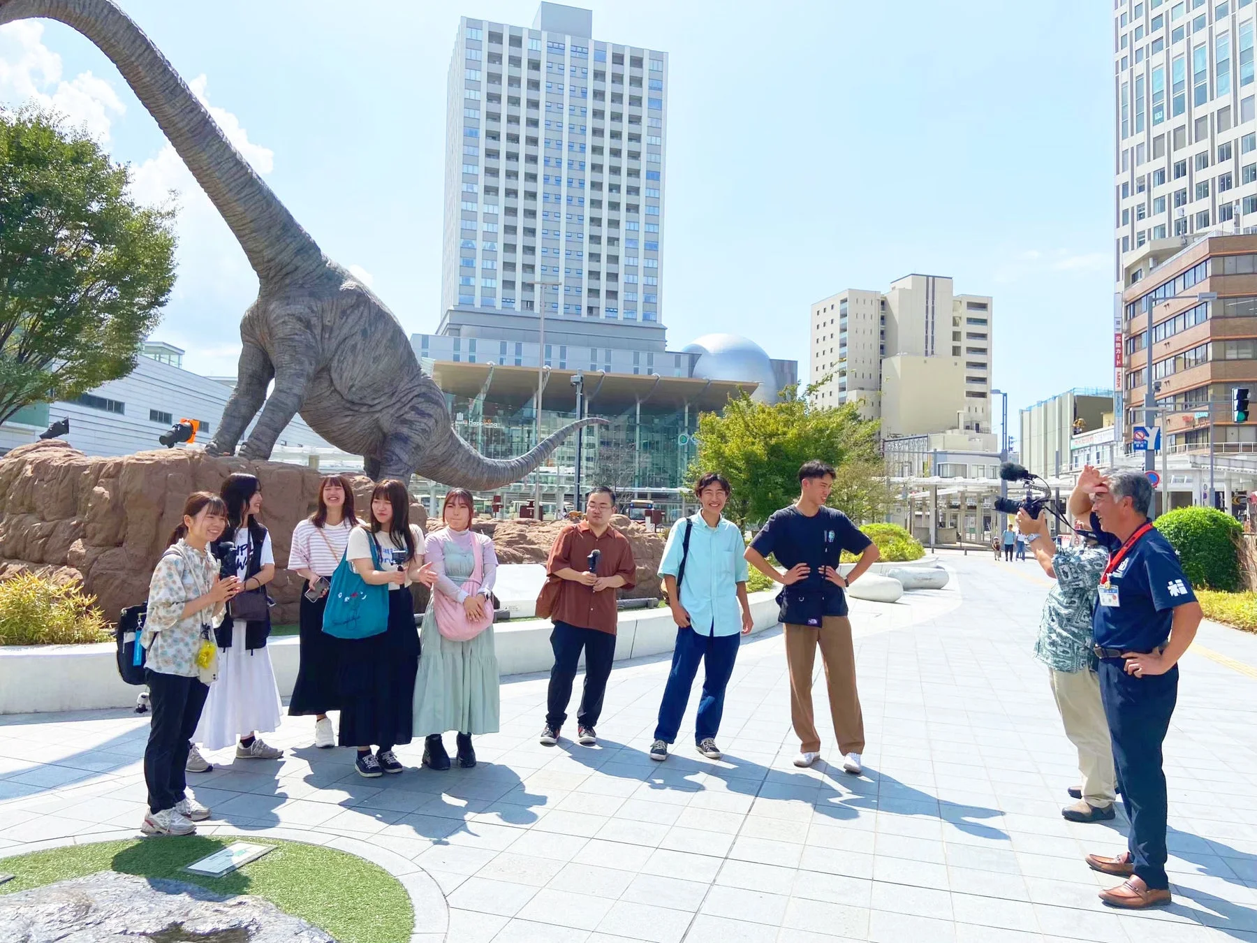 恐竜の像を背景に若者グループが撮影されている様子