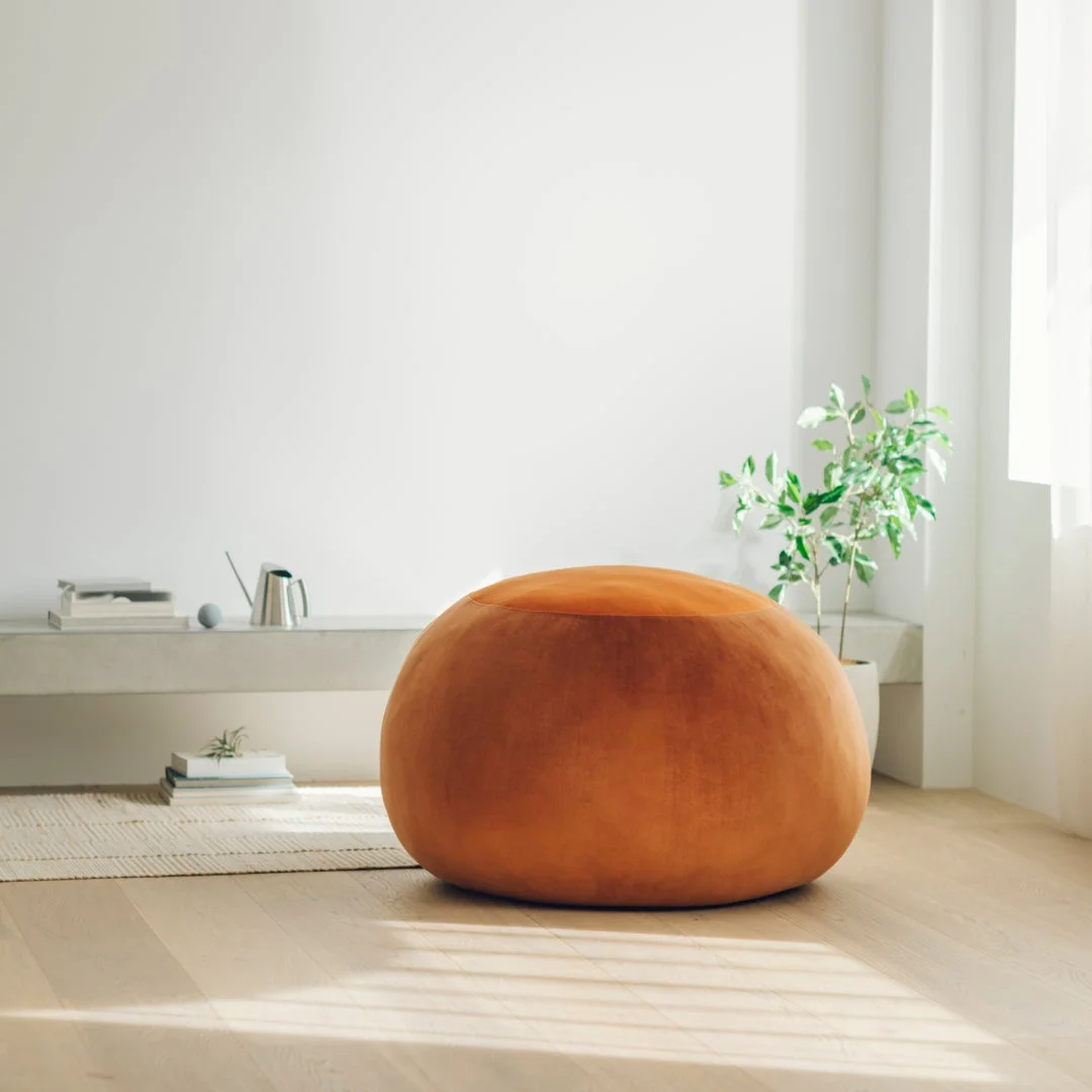 モダンでシンプルな部屋の中央に、丸いオレンジ色のプフが置かれています