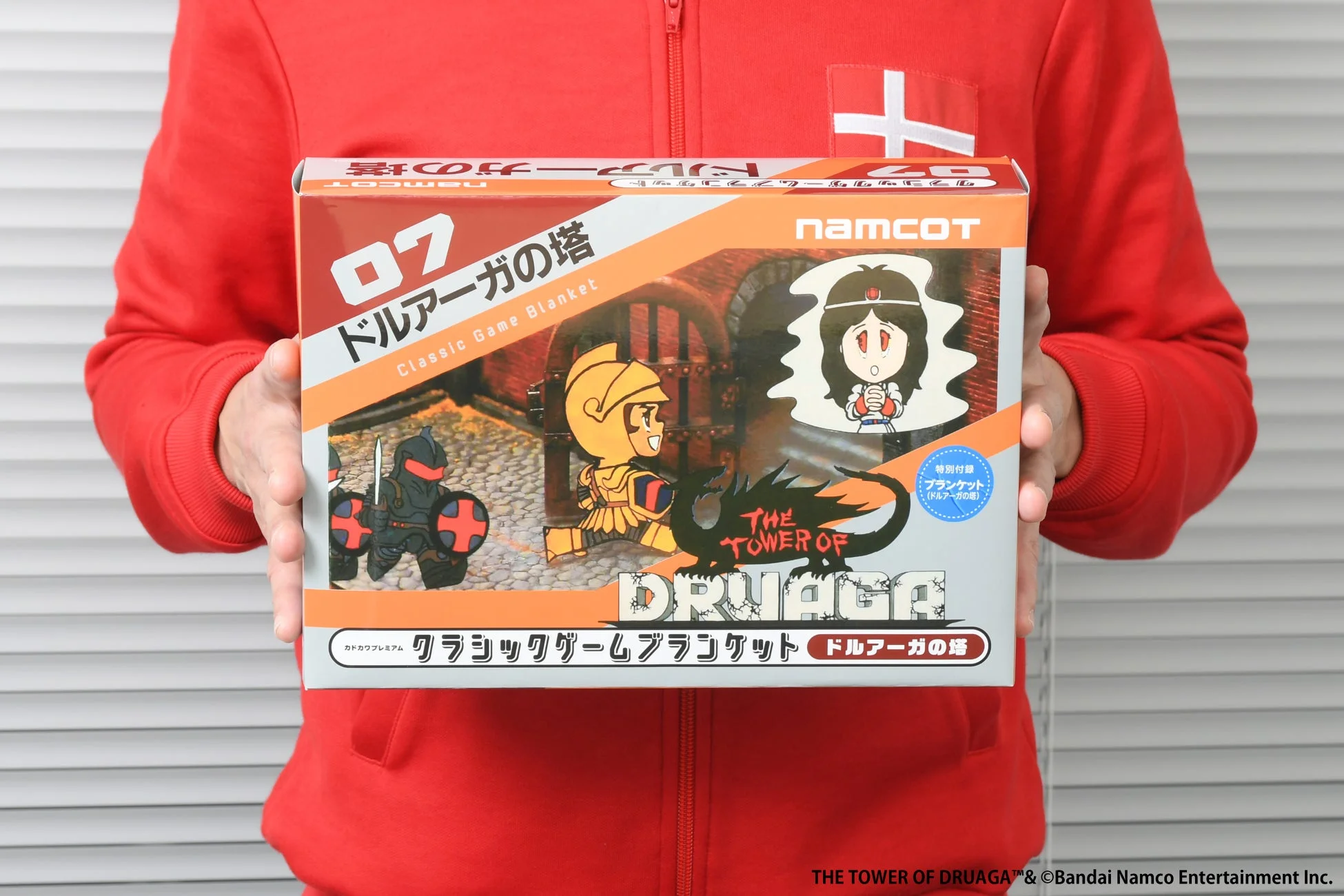 赤いパーカーの人物がドルアーガの塔のブランケットパッケージを持つ