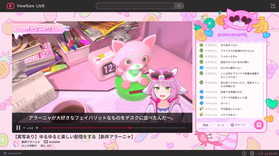 ピンクを基調としたVTuber「新井アラーニャ」のライブ配信画面。デスクに並べられたお気に入りのアイテムを紹介しており、視聴者からのコメントが活発に流れている様子が映し出されている。