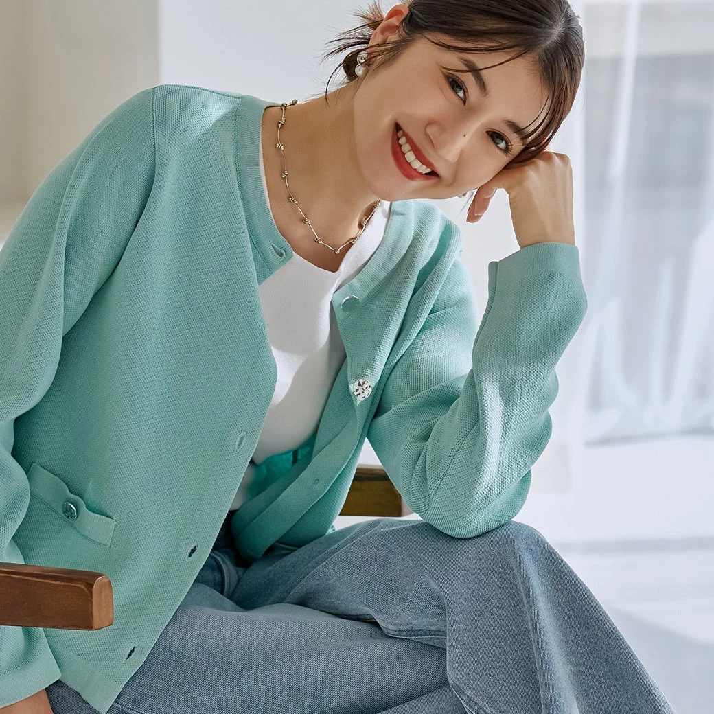 ミントグリーンのカーディガンを着用した女性が、明るい室内で笑顔を見せて座っている様子です