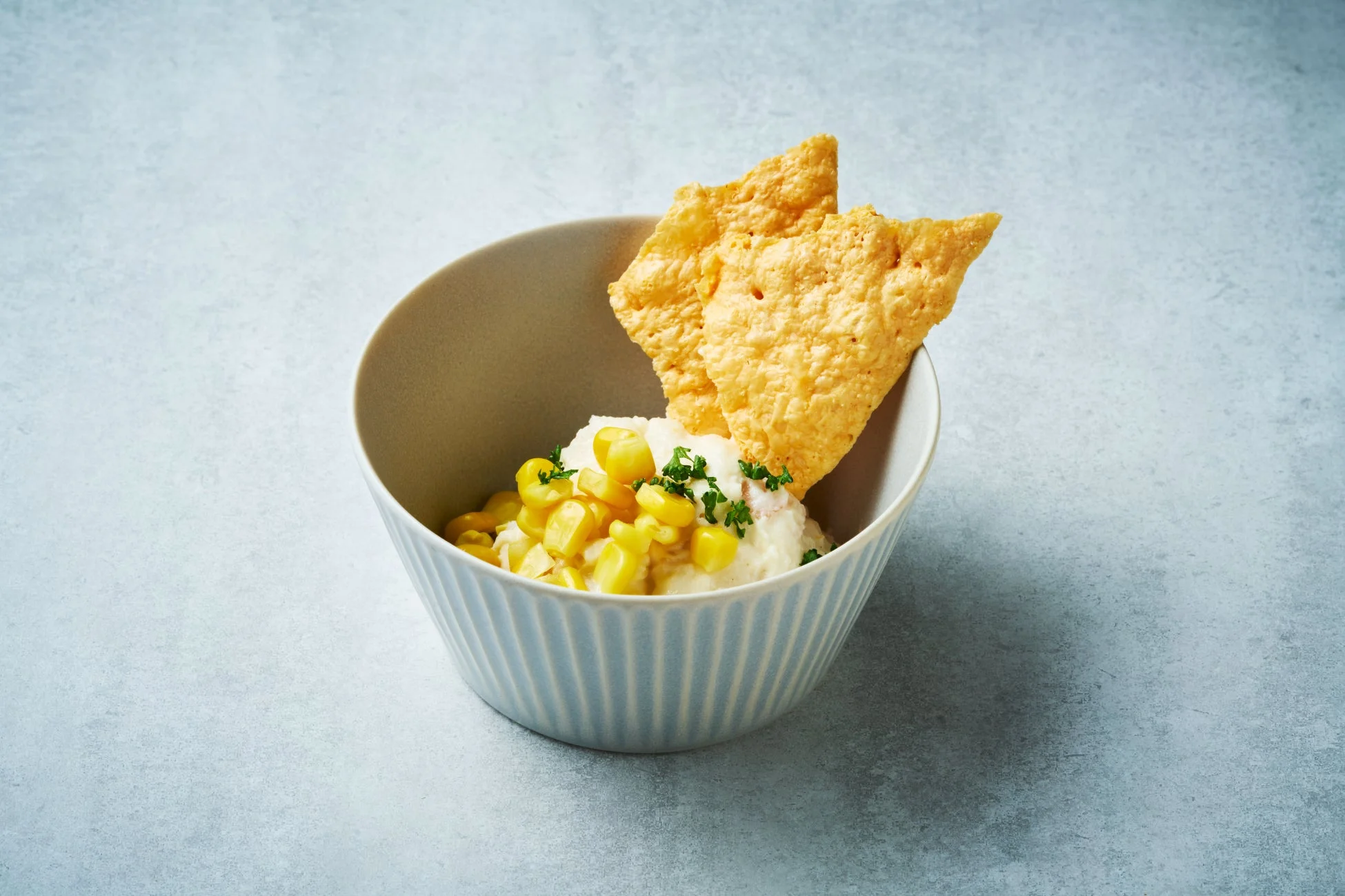 白いクリーム状の料理に黄色いコーンと刻んだハーブがトッピング