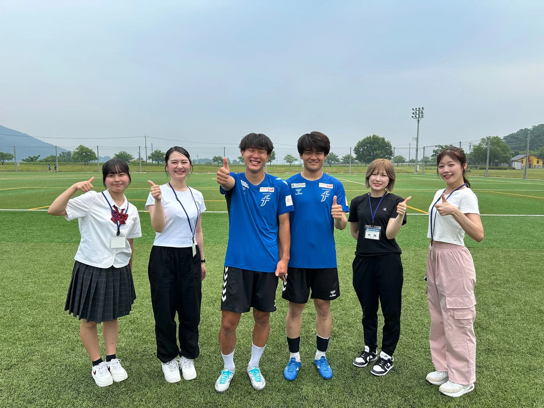 サッカーフィールドで笑顔でサムズアップする集合写真