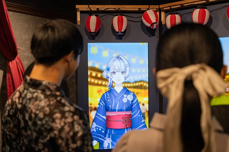 浴衣を着たアニメキャラクターが映し出されたデジタルディスプレイを鑑賞する人々