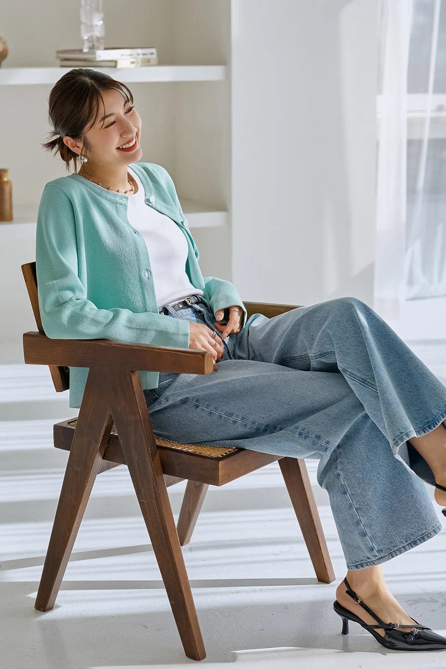 水色のカーディガンとワイドデニムを着用した若い女性が笑顔を見せています