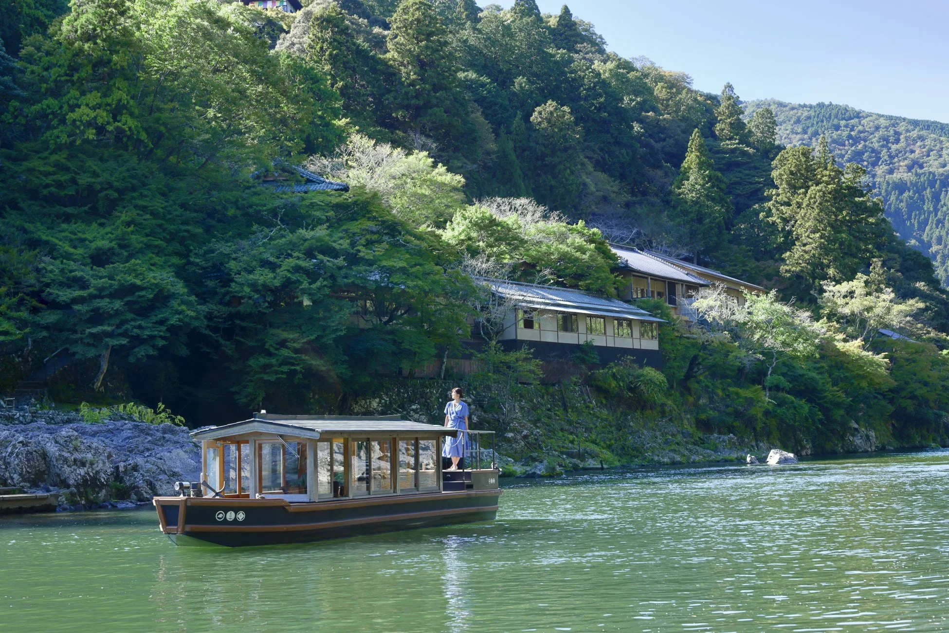 緑豊かな山々と伝統的な建物に囲まれた川を進む遊覧船