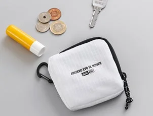 白いポーチが置かれ、その周りに小銭、鍵、黄色のチューブなどの小物が散りばめられた画像