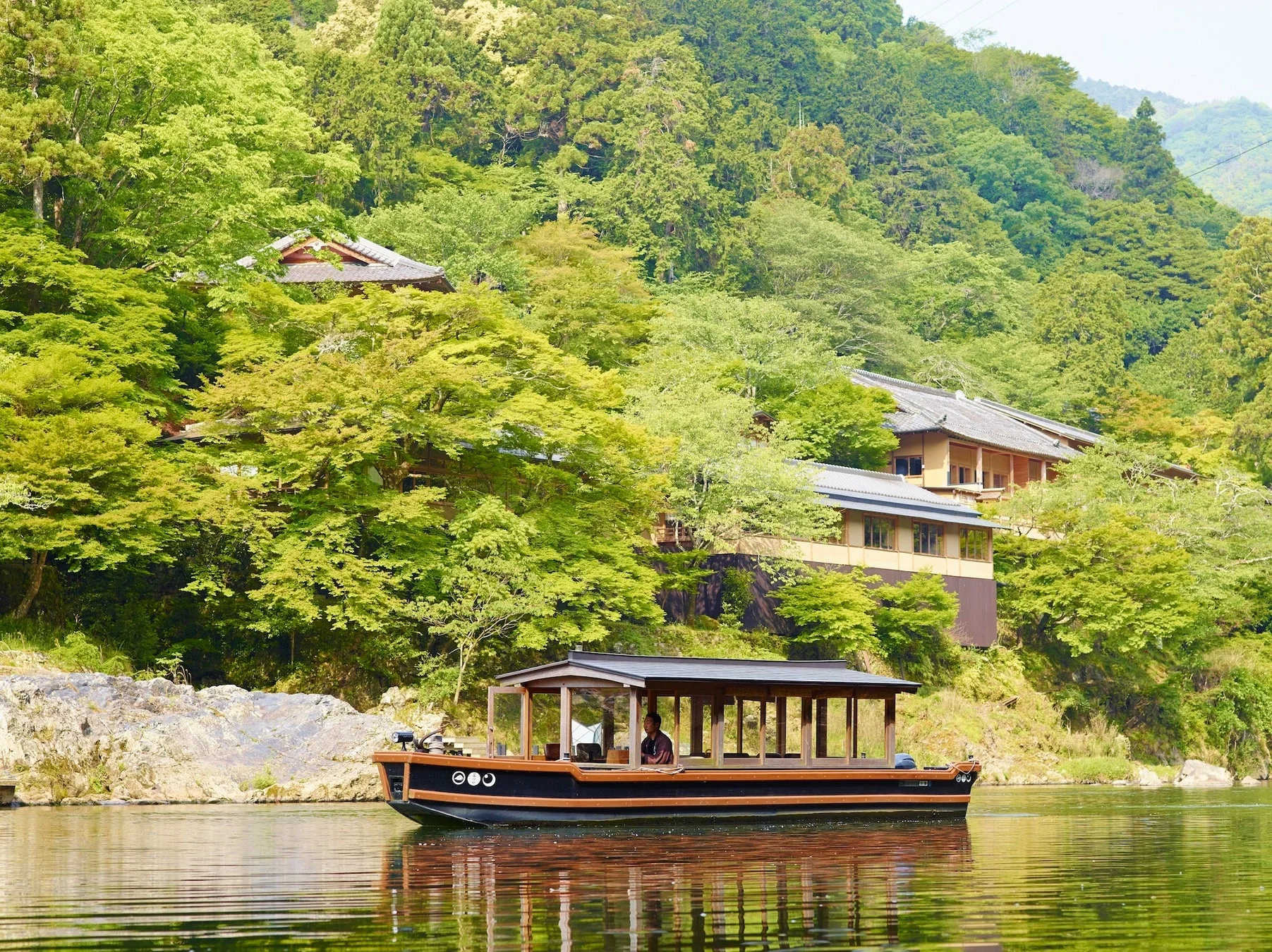新緑の山々に囲まれた川を屋形船が進む日本の風景