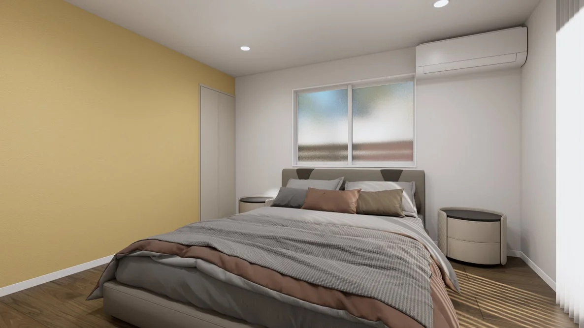 モダンなデザインの寝室で、片方の壁が黄色、他の壁は白く塗られています。広々としたベッドには複数のクッションが置かれ、両脇には丸いナイトテーブルがあります。窓からは柔らかな光が差し込み、天井にはダウンライト、壁にはエアコンが設置されています。