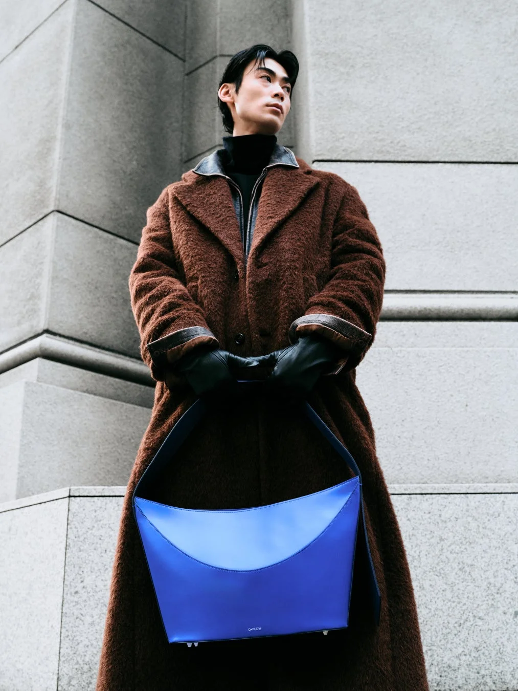 茶色のコートと青いバッグを身につけた男性