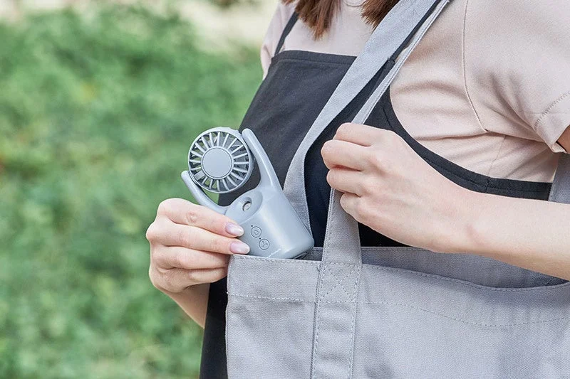 女性がグレーのミスト付き携帯扇風機をトートバッグに入れている。夏の暑い日に持ち運びに便利な冷却アイテムの利用シーン。