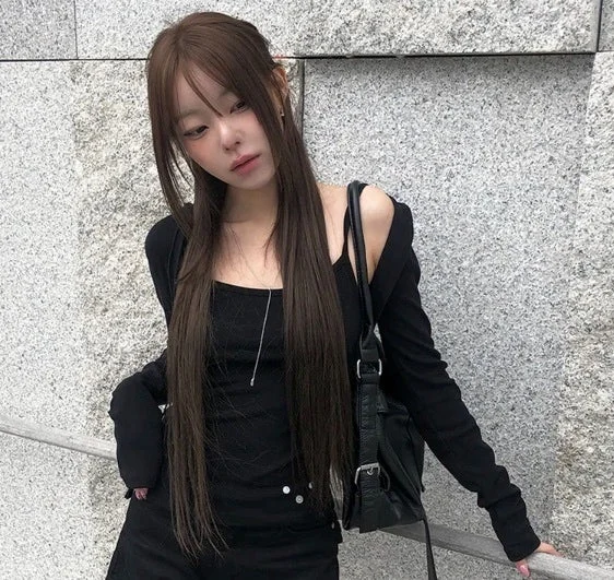 黒いトップスとアウターを着用し、壁を背景にポーズをとる女性