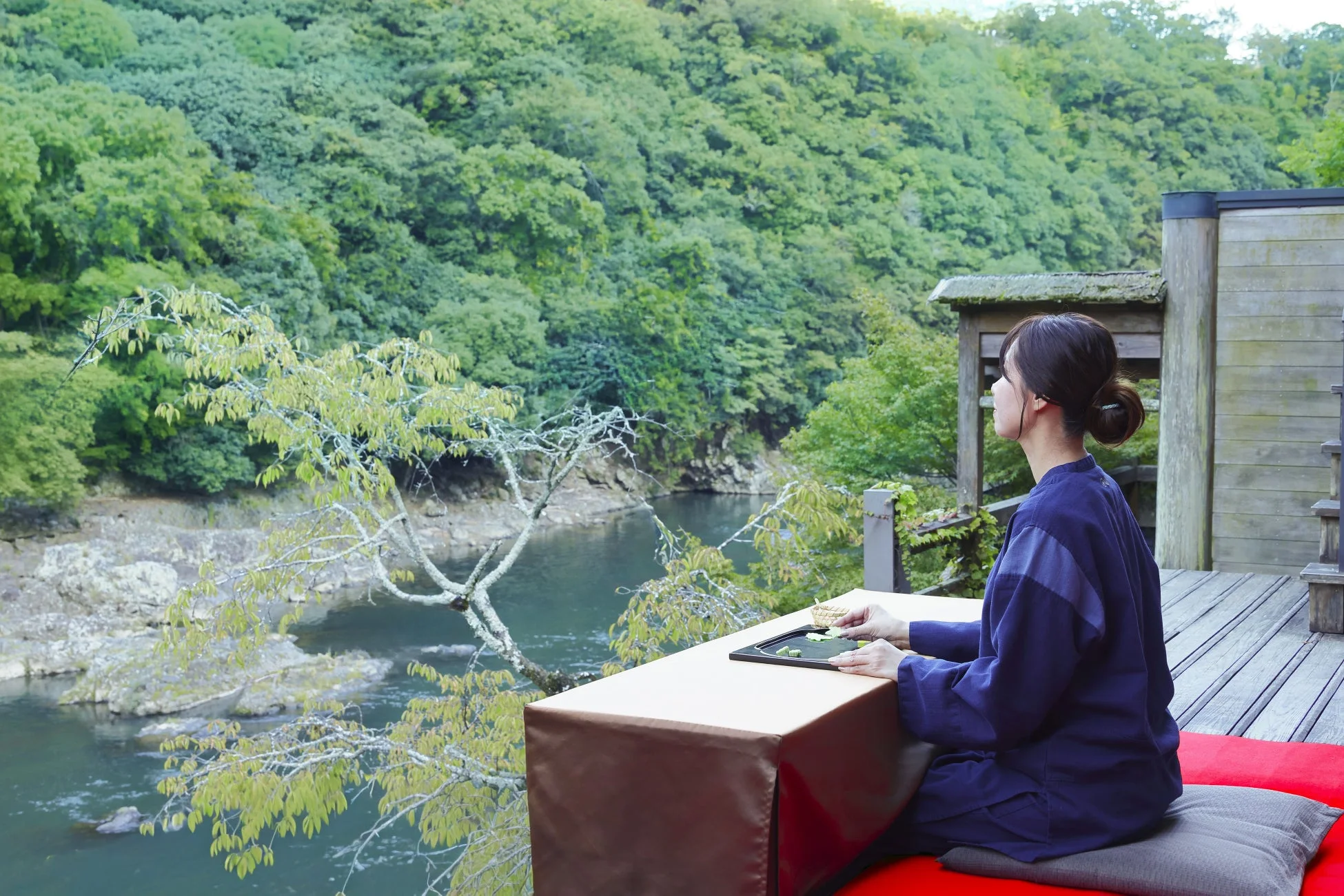 川と緑豊かな山々を望むテラス席でくつろぐ和装の女性