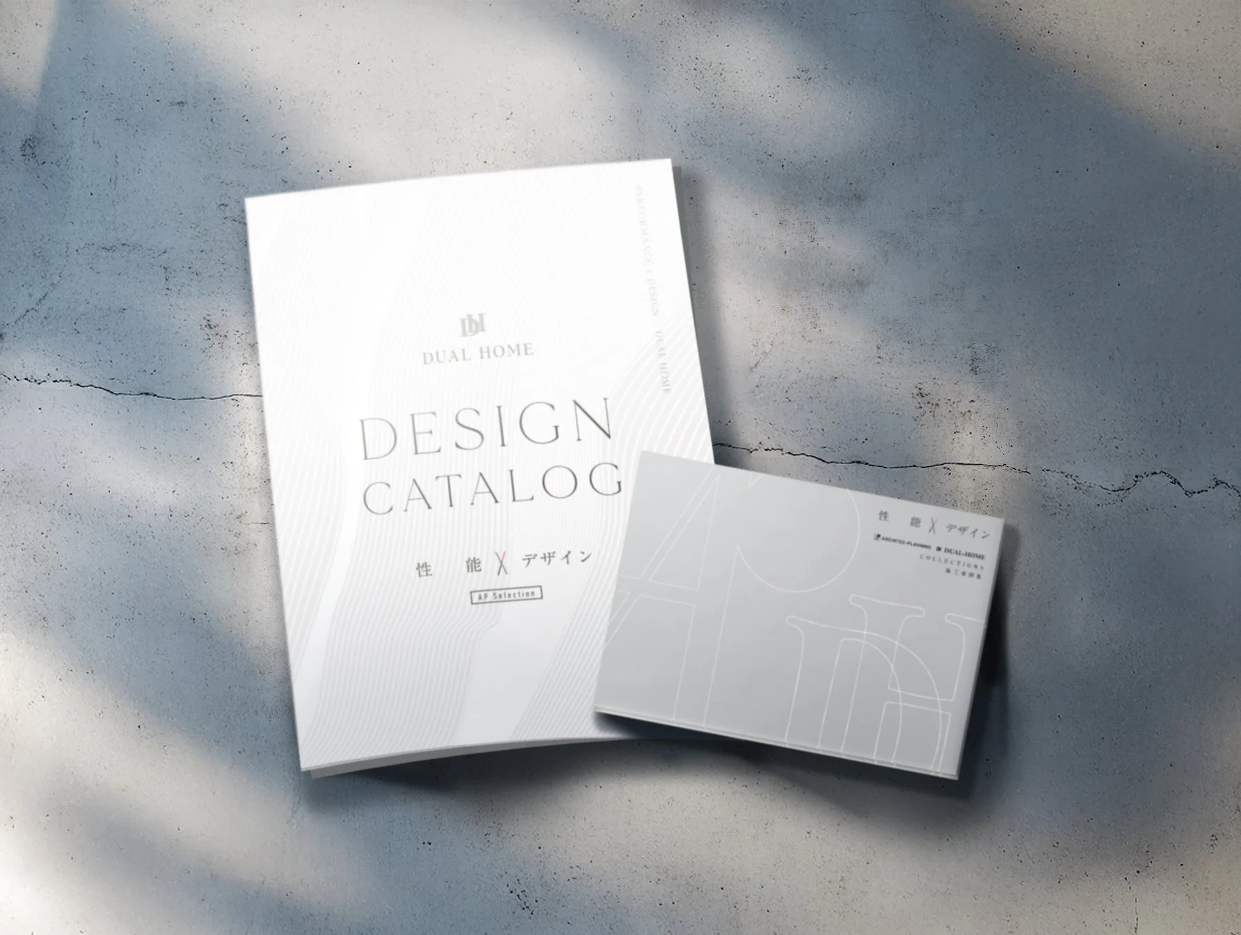 コンクリートの床に置かれた「DUAL HOME」の建築・デザインカタログと施工事例集です。性能とデザインを両立させた住宅関連の資料で、光と影のコントラストが印象的な一枚です。