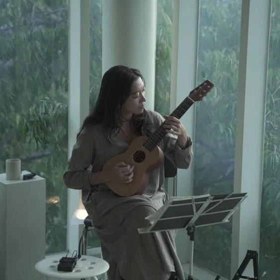 窓の近くでウクレレのような弦楽器を演奏する女性