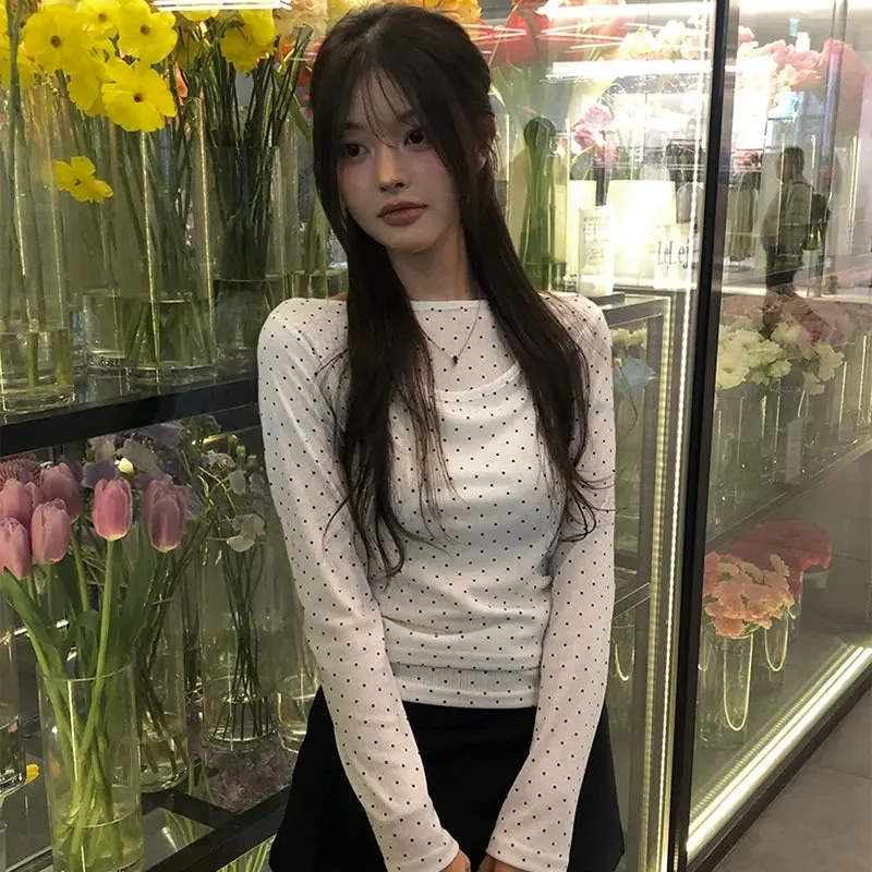 ポルカドット柄の白いトップスと黒いスカートを着用した若い女性が花屋に立つ