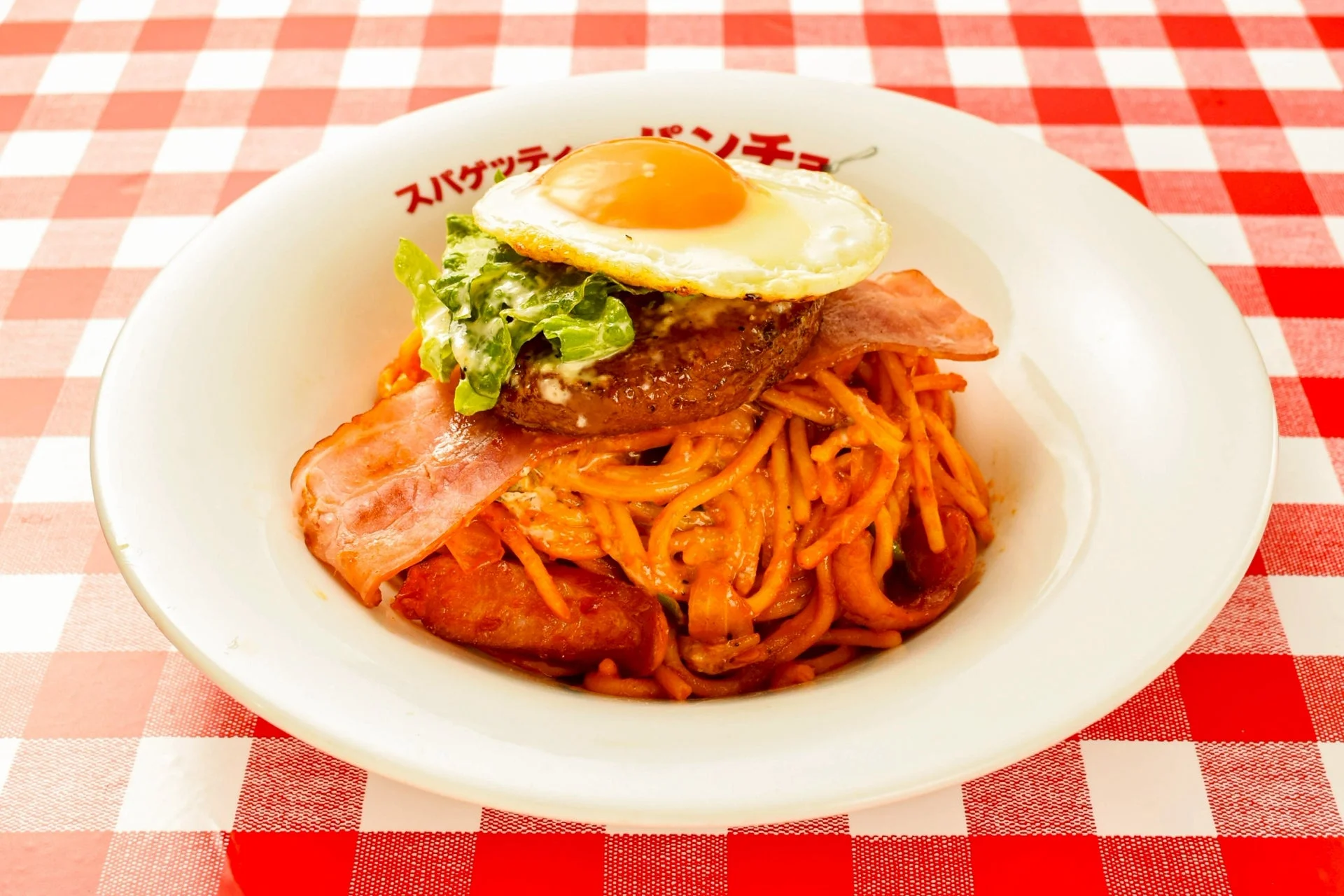 目玉焼き、ハンバーグ、ベーコン、レタスなどが豪華に盛り付けられたナポリタンスパゲッティのクローズアップ画像