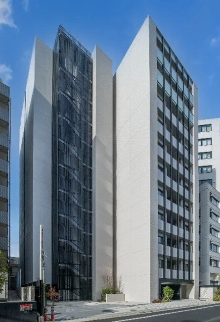 青空の下に建つ、現代的でスタイリッシュな高層ビル。白い外壁と、黒い格子状の装飾が施された特徴的なデザインが目を引きます。