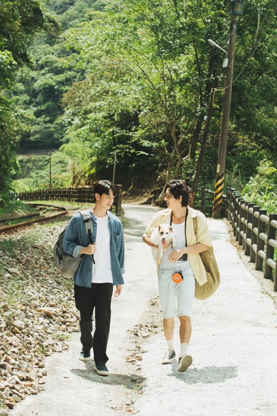 緑豊かな自然の中、線路沿いの小道を2人の男性が愛犬を連れて散歩している様子