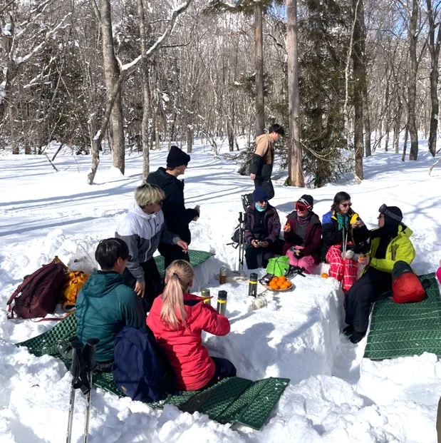 雪深い森の中で、友人たちが集まって冬のピクニックを楽しんでいる様子