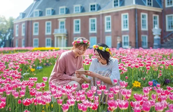 女性二人,花冠,チューリップ,花畑,春,笑顔,スマートフォン,公園,屋外,観光,旅行,ヨーロッパ風建築