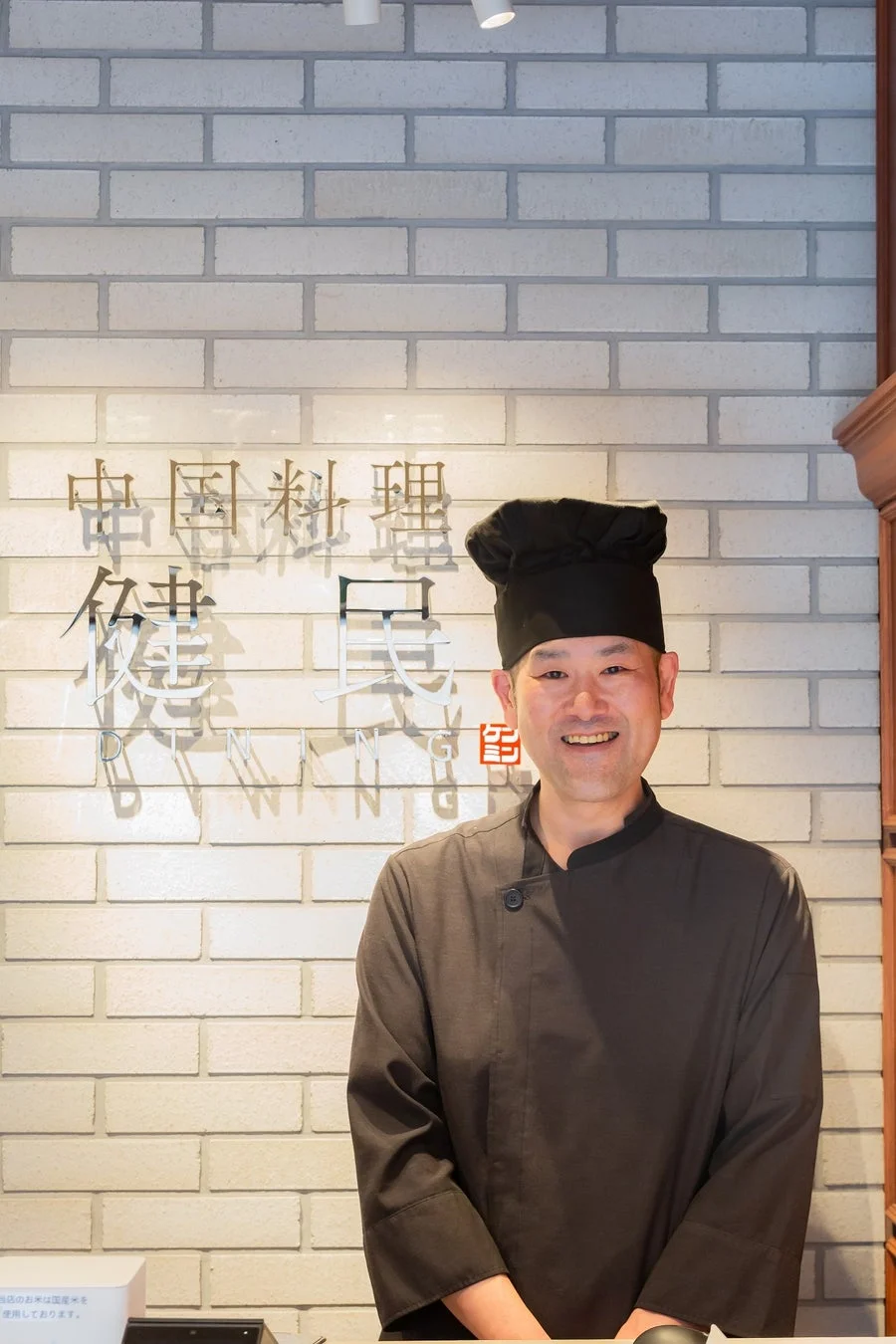 黒いシェフ帽と制服を着て笑顔で立つ男性料理人