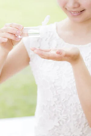 白い服を着た女性が、透明なボトルに入ったクリアな液体を手のひらに注いでいます。