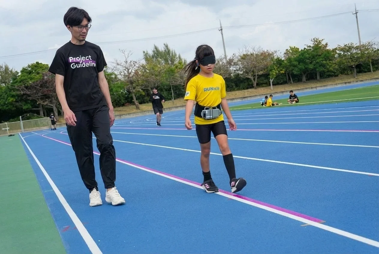 目隠しをした少女がProject Guidelineのサポートで歩行練習をしている様子