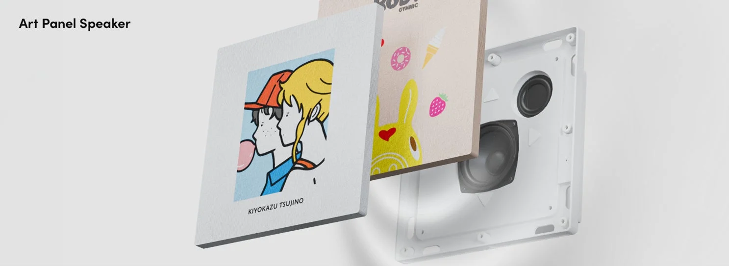アートパネルスピーカーの製品画像で、交換可能なアートパネルが複数枚重ねて表示されています。手前のパネルにはカートゥーン調の人物イラストが描かれ、奥には可愛らしい模様のパネルと、スピーカー本体の内部構造が見えています。