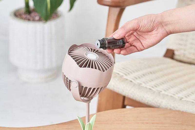 卓上ミニファンにローズウッドのアロマオイルを垂らしている様子。アロマディフューザーとしても使えるピンク色のファンが、心地よい香りで空間を演出します。