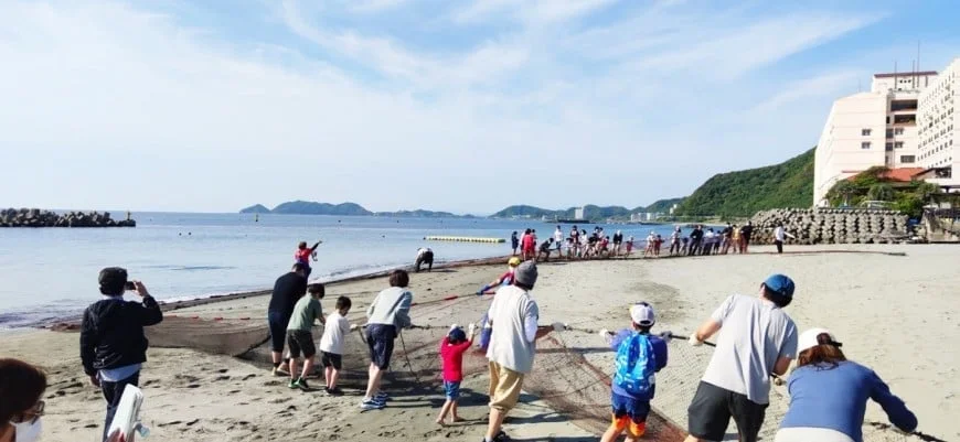 ビーチで地引網漁を体験する家族連れ