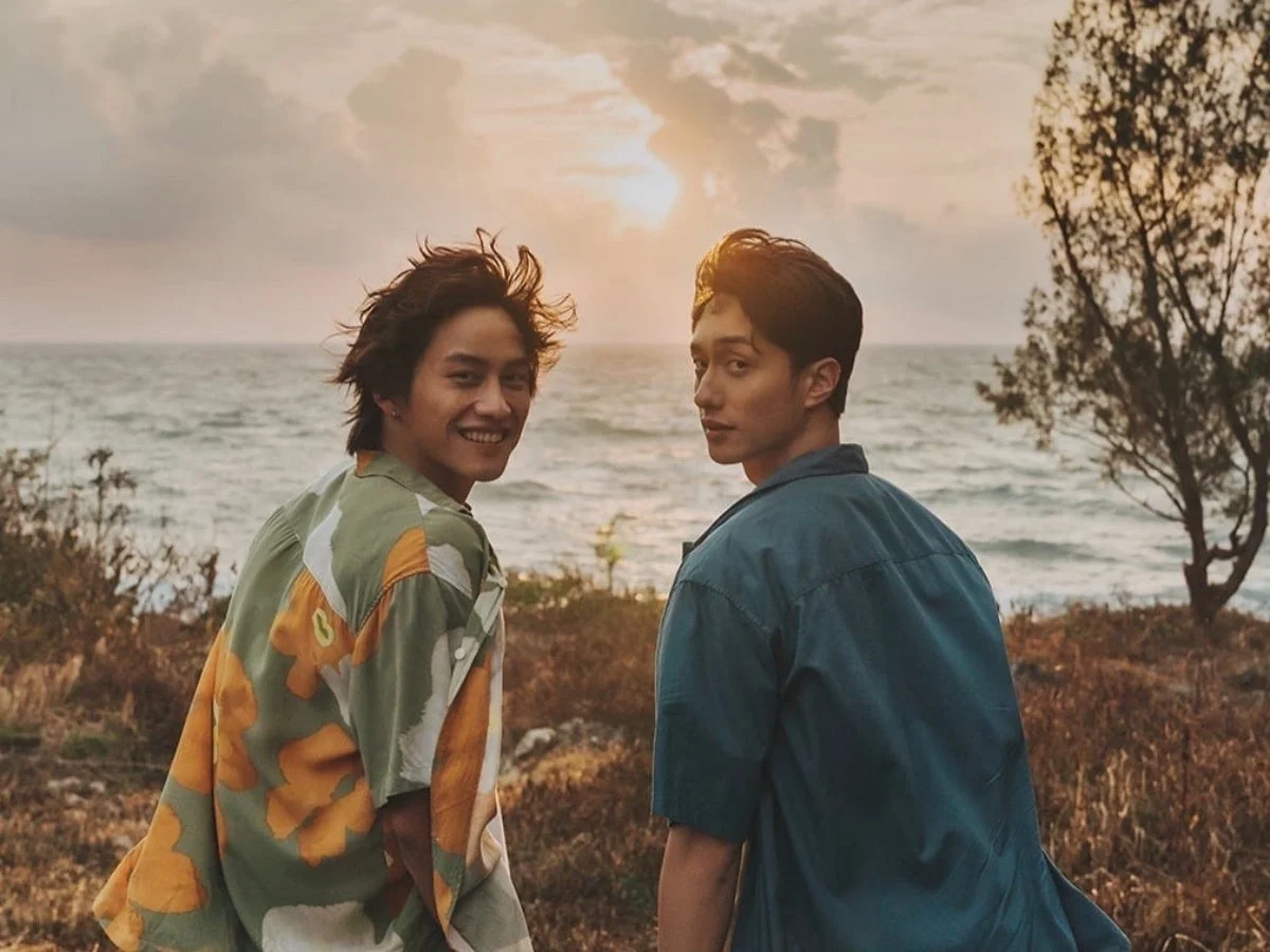 夕焼けの海辺で二人の男性がカメラを振り返っている様子