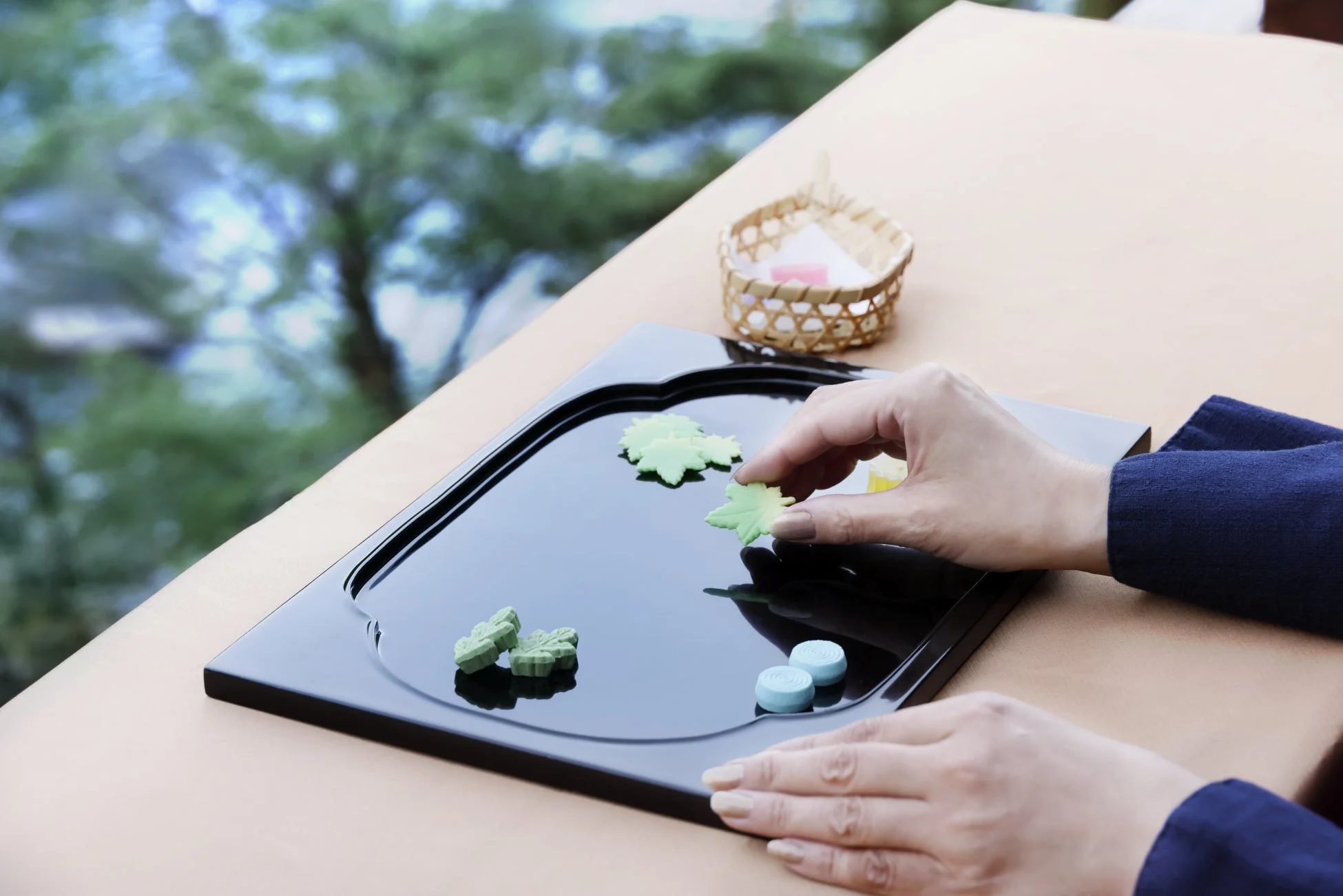 黒いトレイの上で葉の形をした和菓子を並べる手