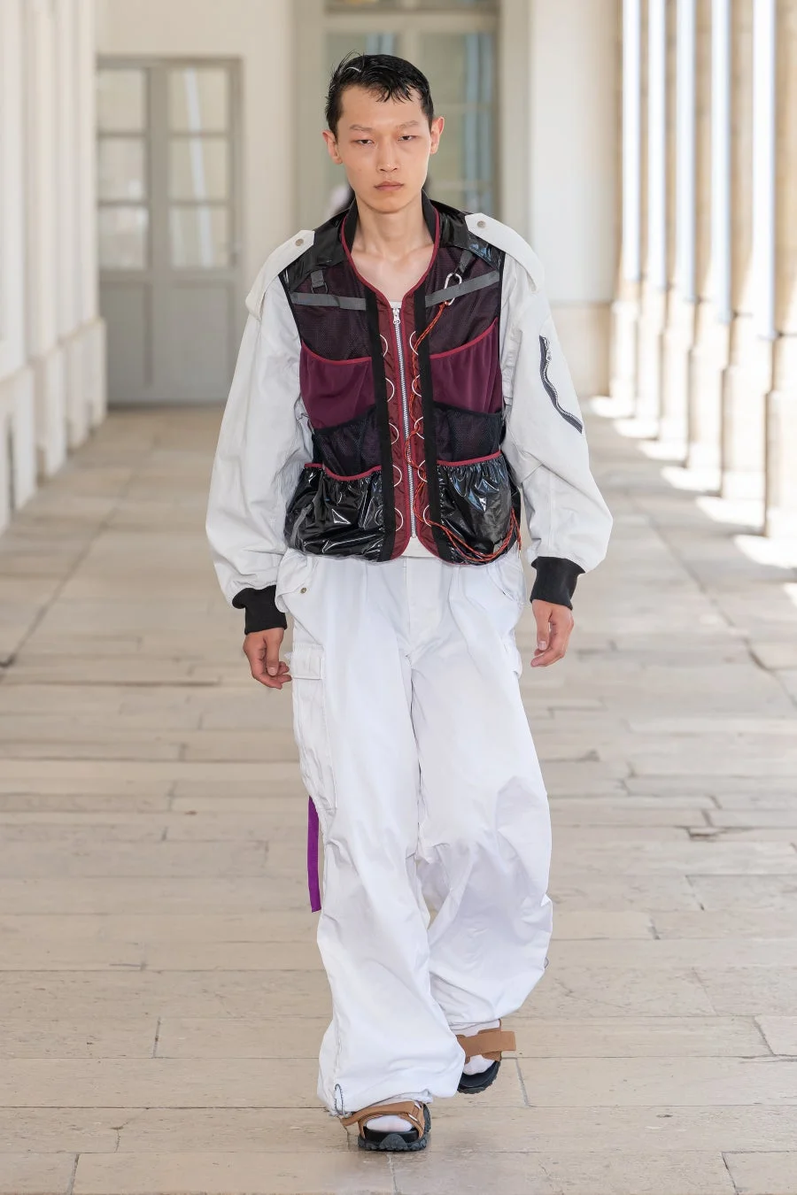 多機能ベストと白いカーゴパンツを合わせた個性的なレイヤードスタイルの男性モデル