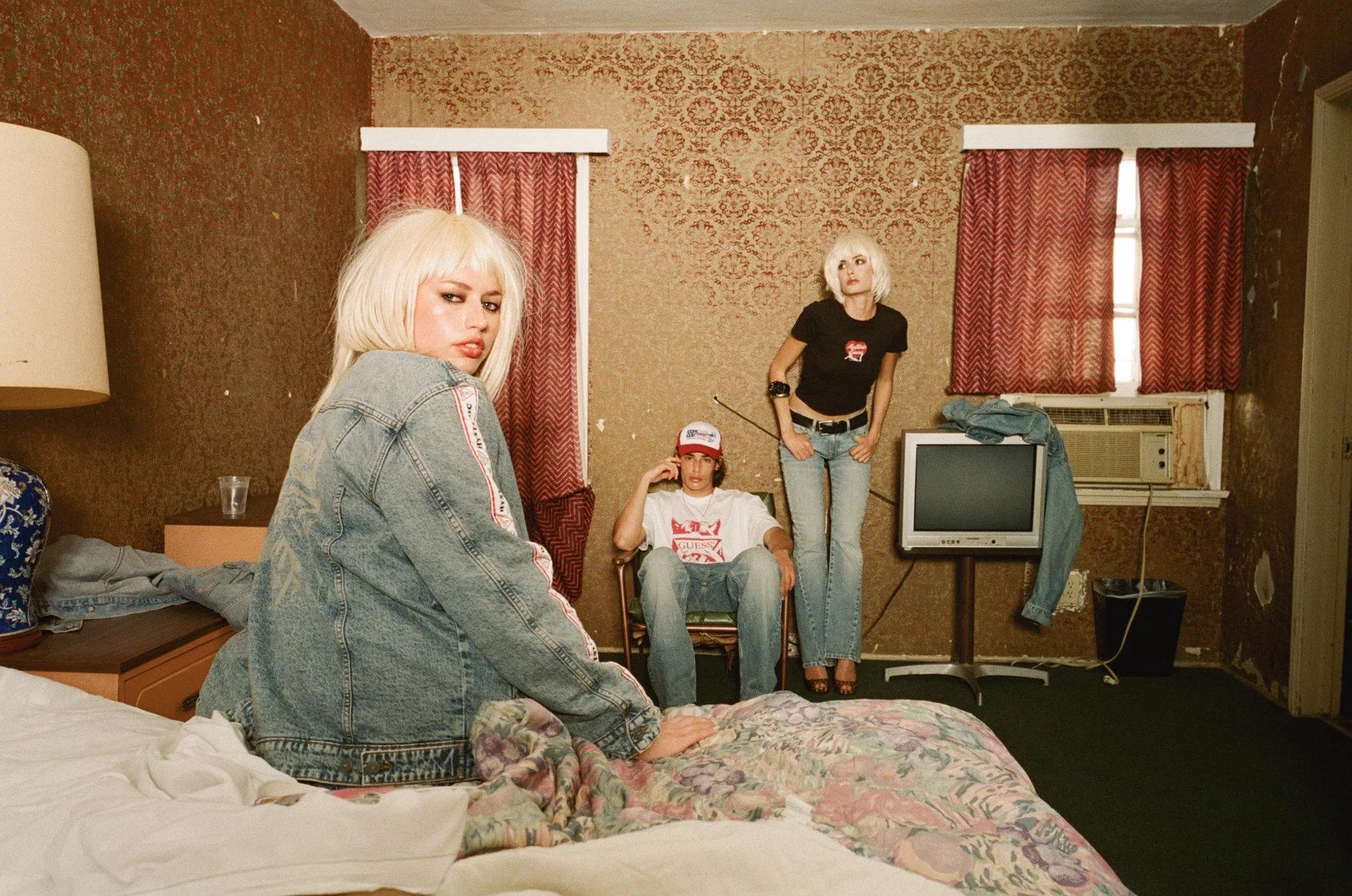 90年代ファッション、Y2K、レトロ、ヴィンテージ、若者、ホテル、モーテル、デニムジャケット、ブロンドヘア、ファッション写真、アート写真、室内、ベッド、テレビ、エアコン、グランジ