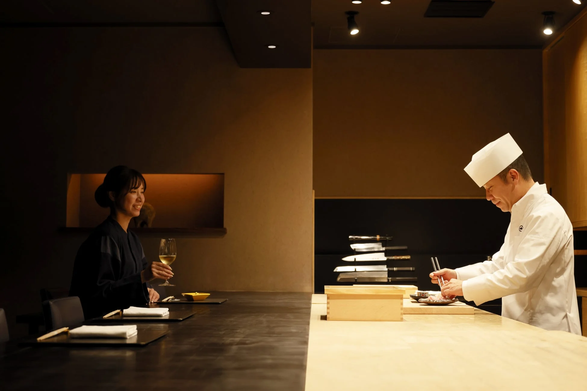 高級感のある日本料理店で食事を楽しむ女性と料理を盛り付けるシェフ