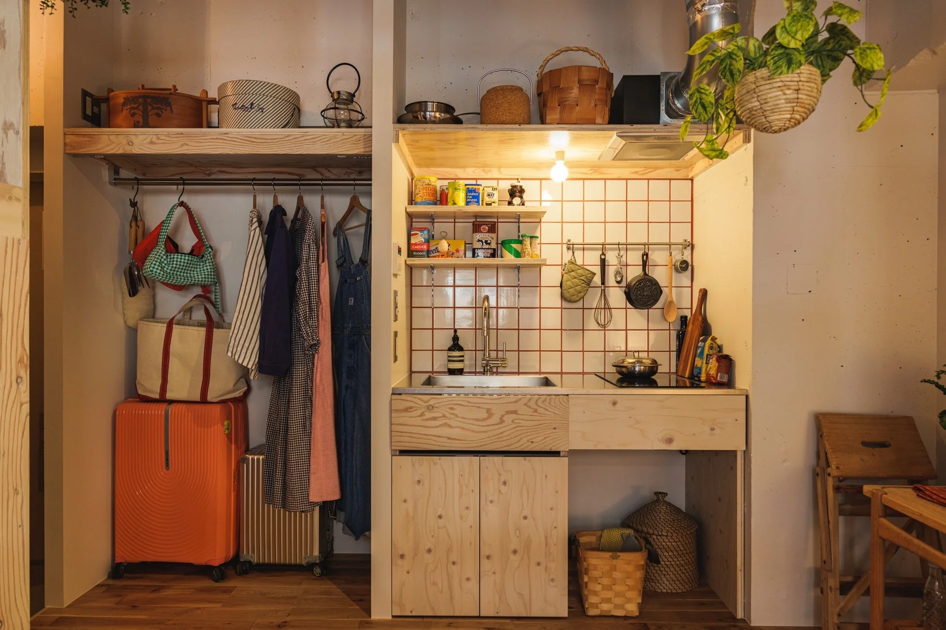 コンパクトな空間に、衣類やスーツケースを収納したオープンクローゼットと、白と赤のタイルが特徴的な小さなキッチンが並んでいます。
