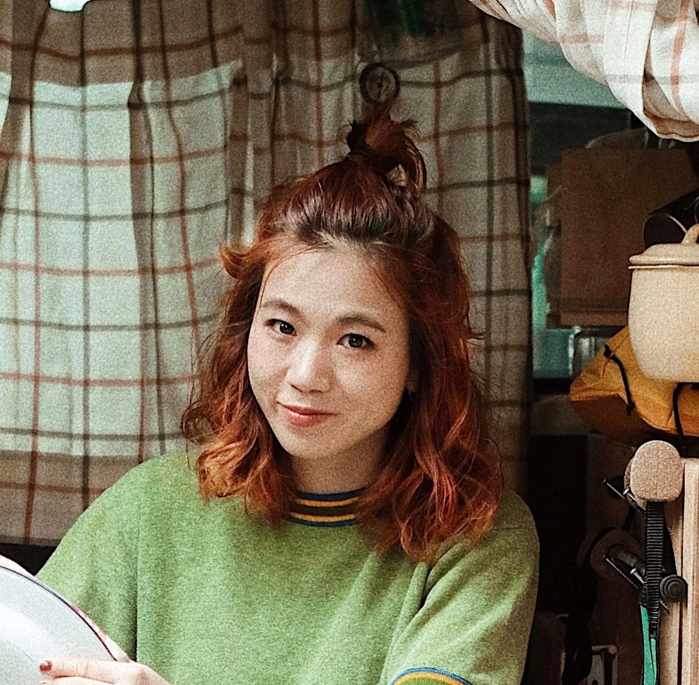 赤みがかった茶色の髪の若い女性が、緑色のセーターを着てカメラに向かって微笑んでいます。