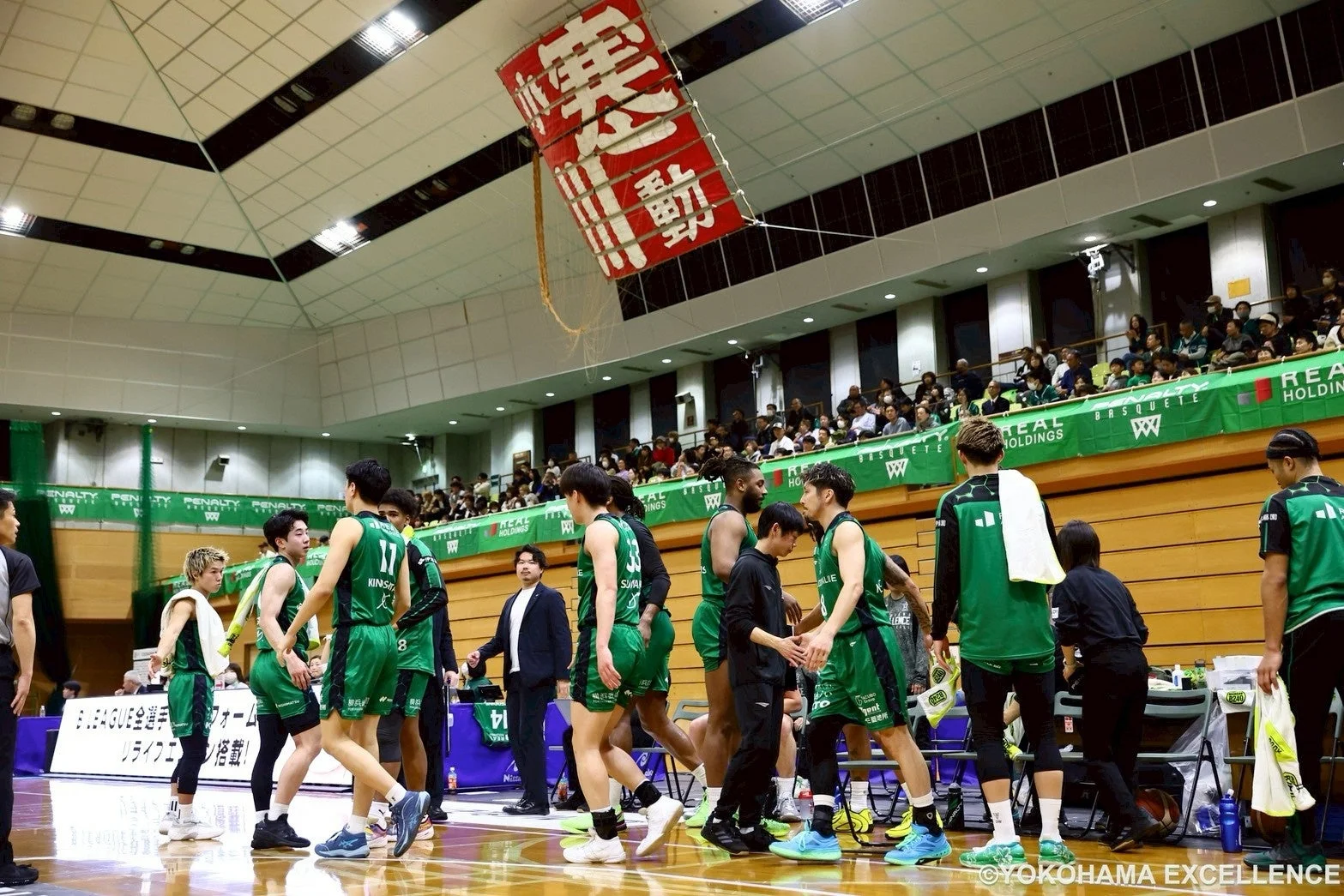 バスケットボールのアリーナで、緑色のユニフォームを着た選手たちがコートに集まっている