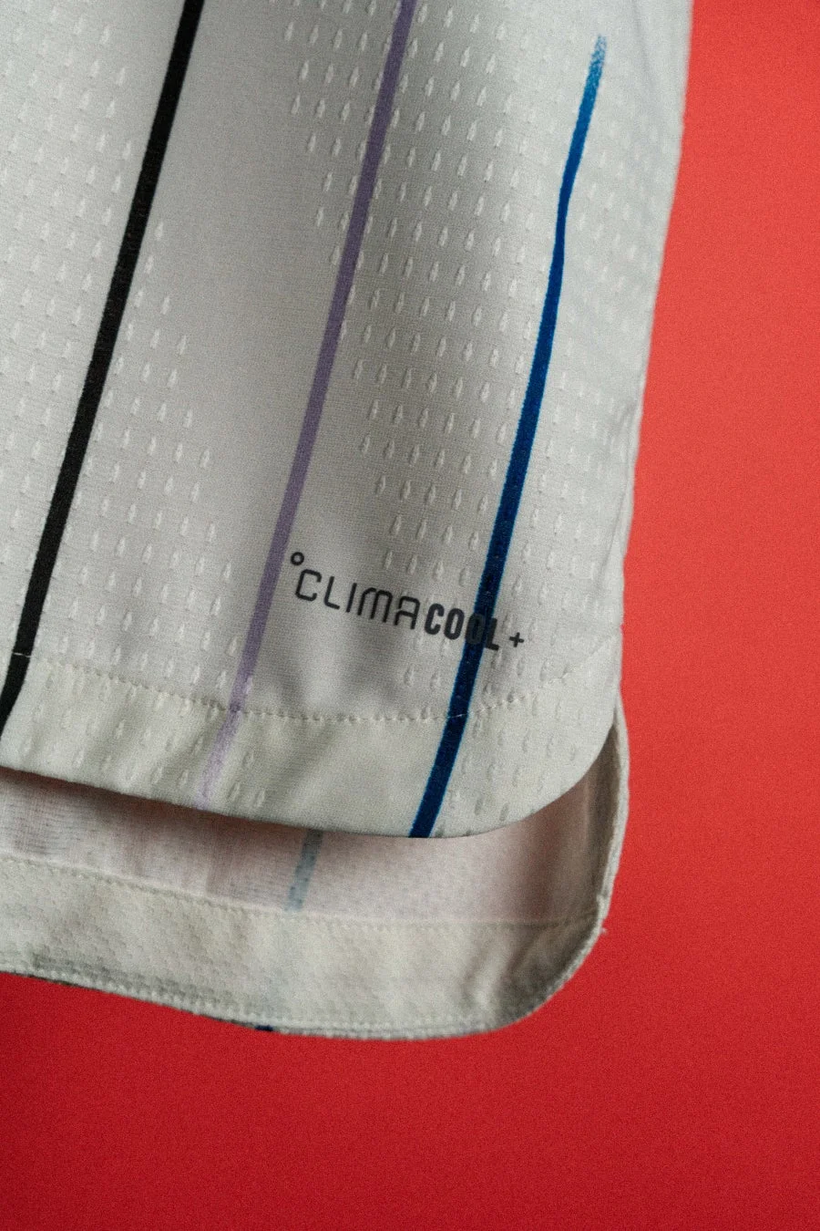 白いスポーツウェアの生地をクローズアップした画像で、黒、紫、青の縦縞模様が見られます。生地には「CLIMACOOL+」のロゴがあり、速乾性などの機能素材であることを示唆しています。