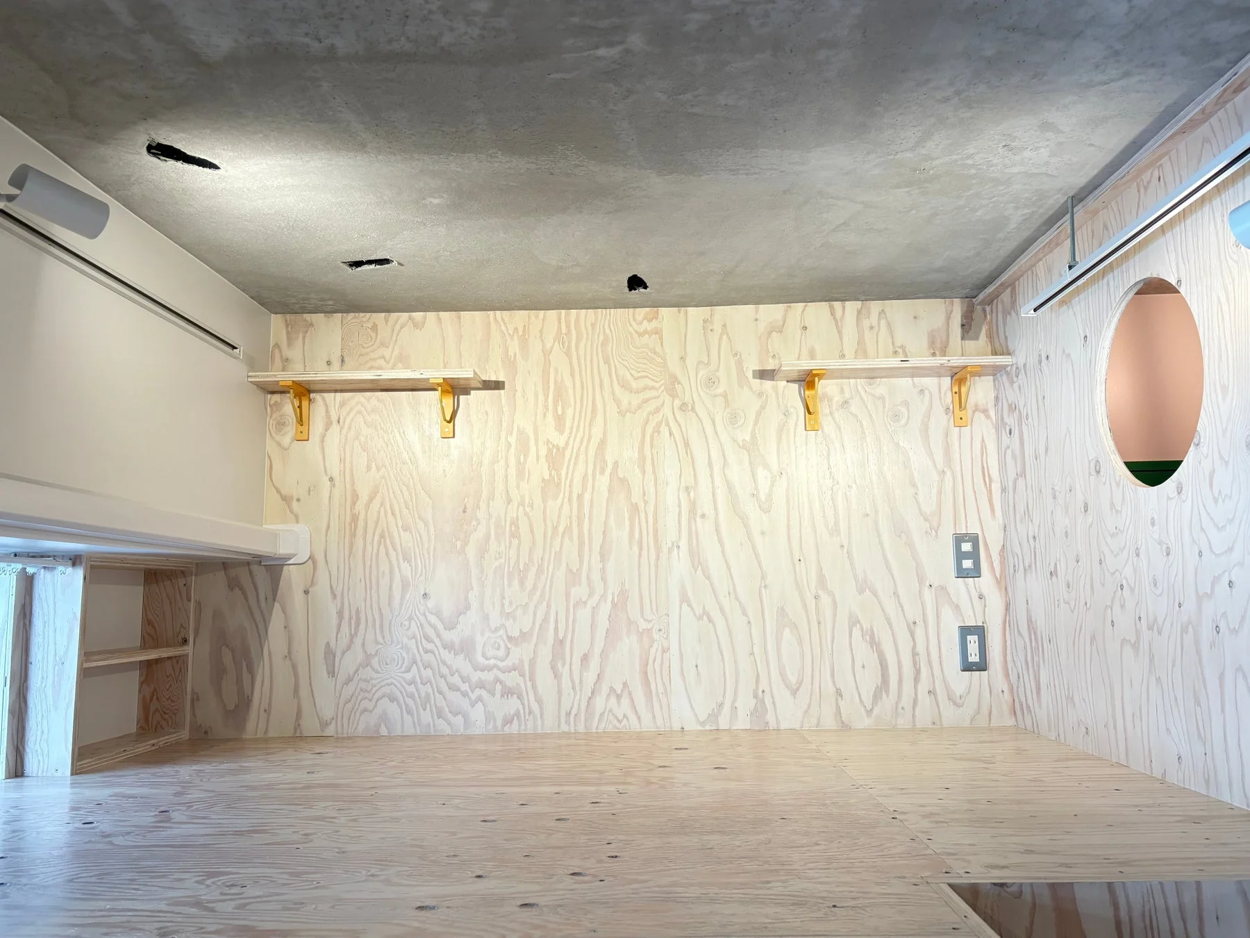 合板の壁と床、棚が特徴の室内空間