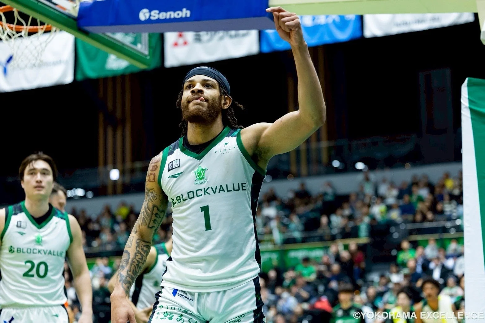 バスケットボールの試合中、背番号1の選手が白いユニフォームを着て片腕を上げ、ガッツポーズをしている様子。アリーナには観客が見え、熱気あふれる瞬間を捉えている。