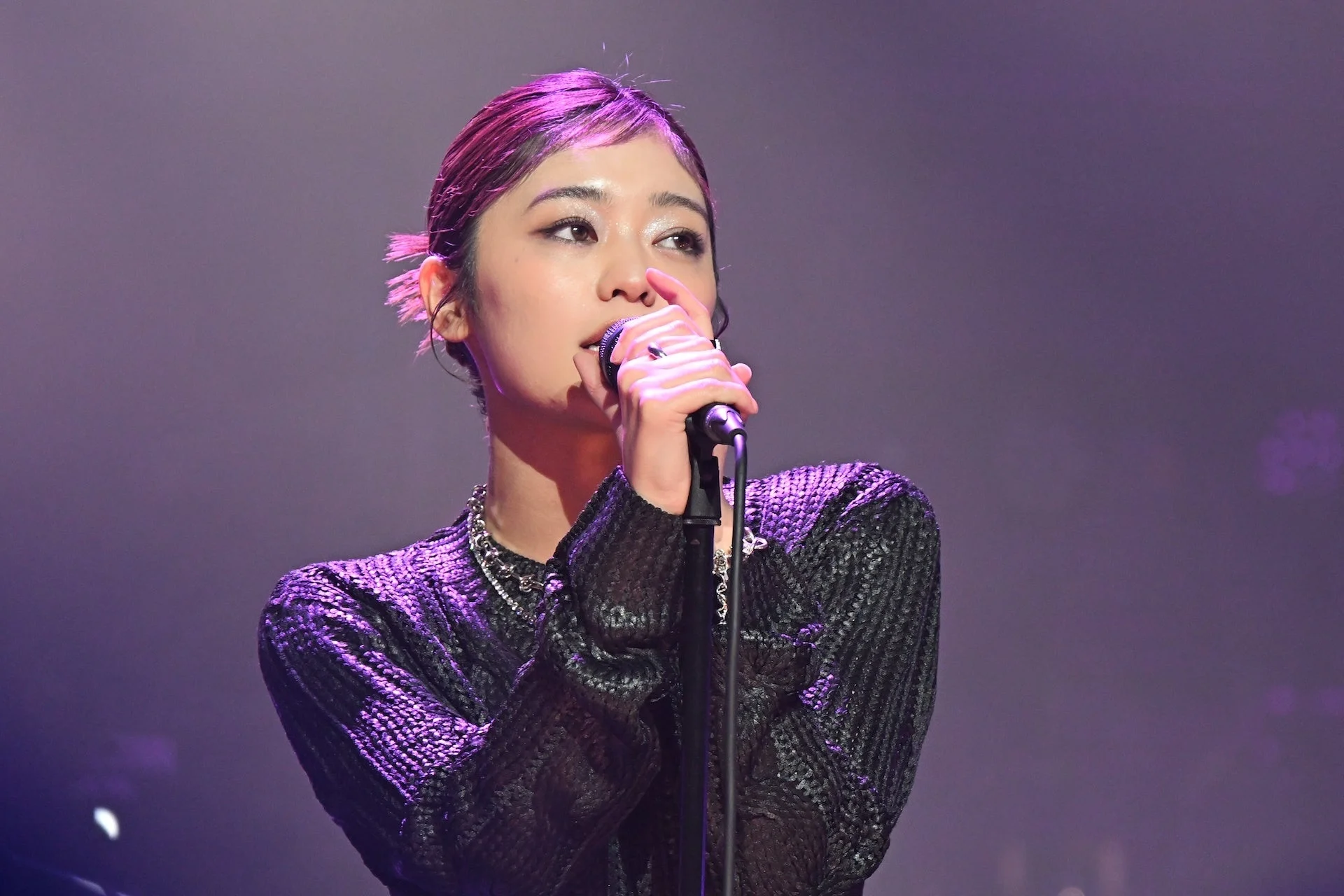 紫色の照明が当たるステージでマイクを握り歌唱する吉柳咲良