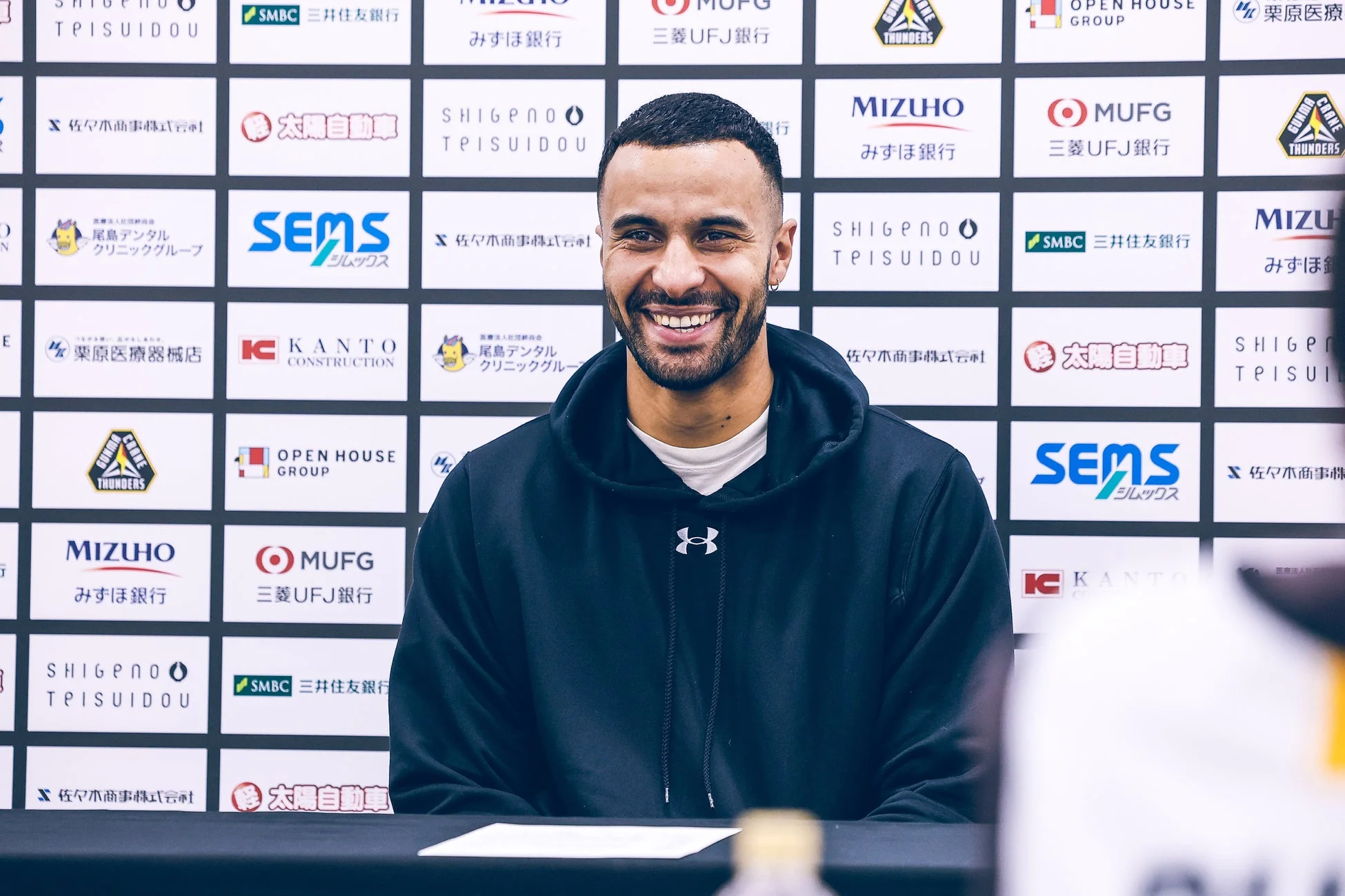スポンサーロゴが並ぶ背景の前で笑顔を見せる群馬クレインサンダーズのヨハネス・ティーマン選手