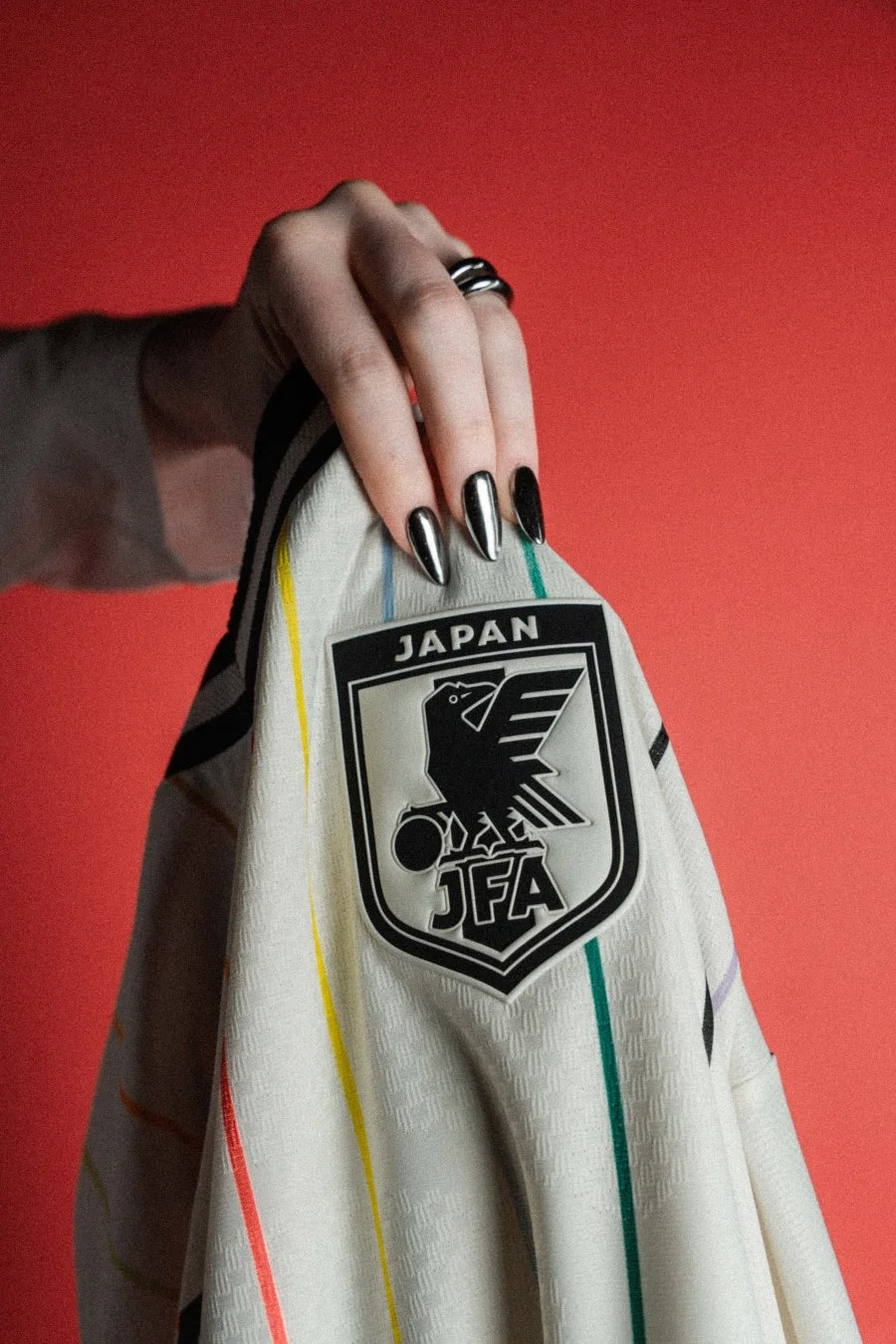 JFAロゴとカラフルなストライプが入った日本代表の白いユニフォームを掴んでいる様子